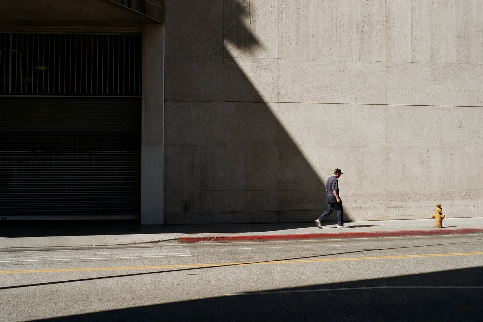 A pedestrian crossing a bright concrete wall divided by a deep diagonal shadow