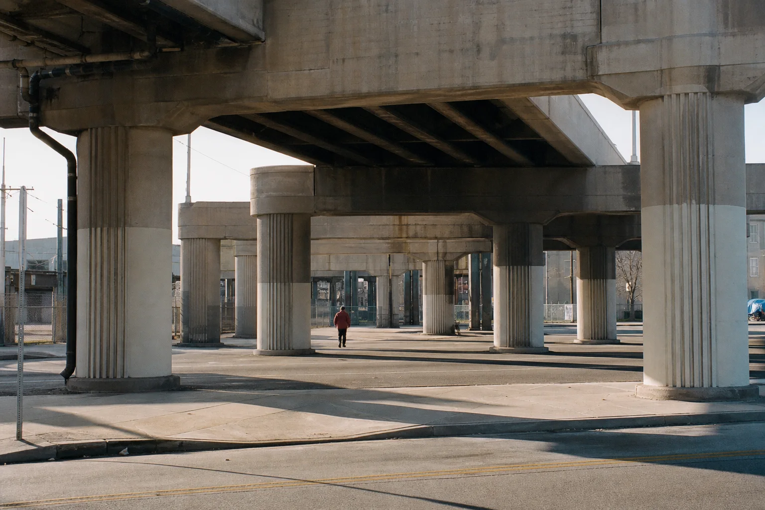 A distant person in a red jacket walking beneath repeating freeway columns